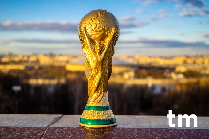 A world cup trophy placed on a railing overlooking a city skyline.